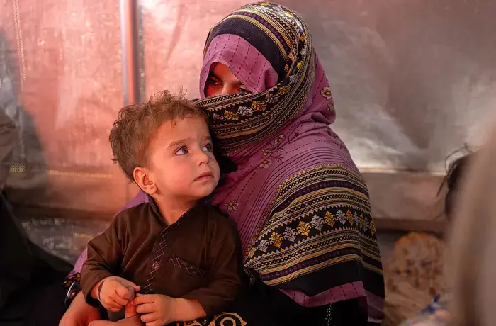 An Afghan woman, who returned from Pakistan earlier that day, rests with her son inside a tent erected to give returnees some shade from the burning sun at Takhta Pul, near the Pakistan border. UN Women: Sayed Habib Bidell.